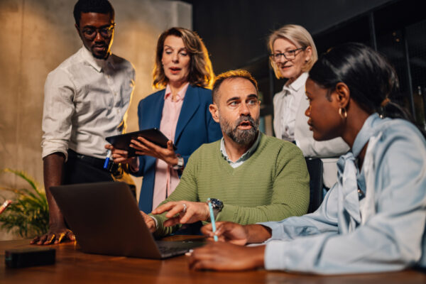 A group of men and women discuss something around a laptop