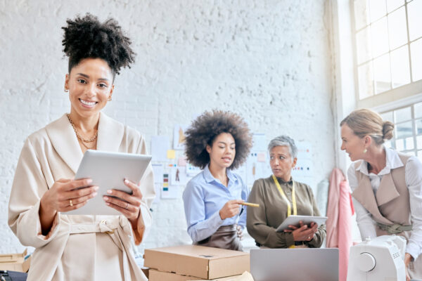 Four people stand in a small business shop using tablets and computers